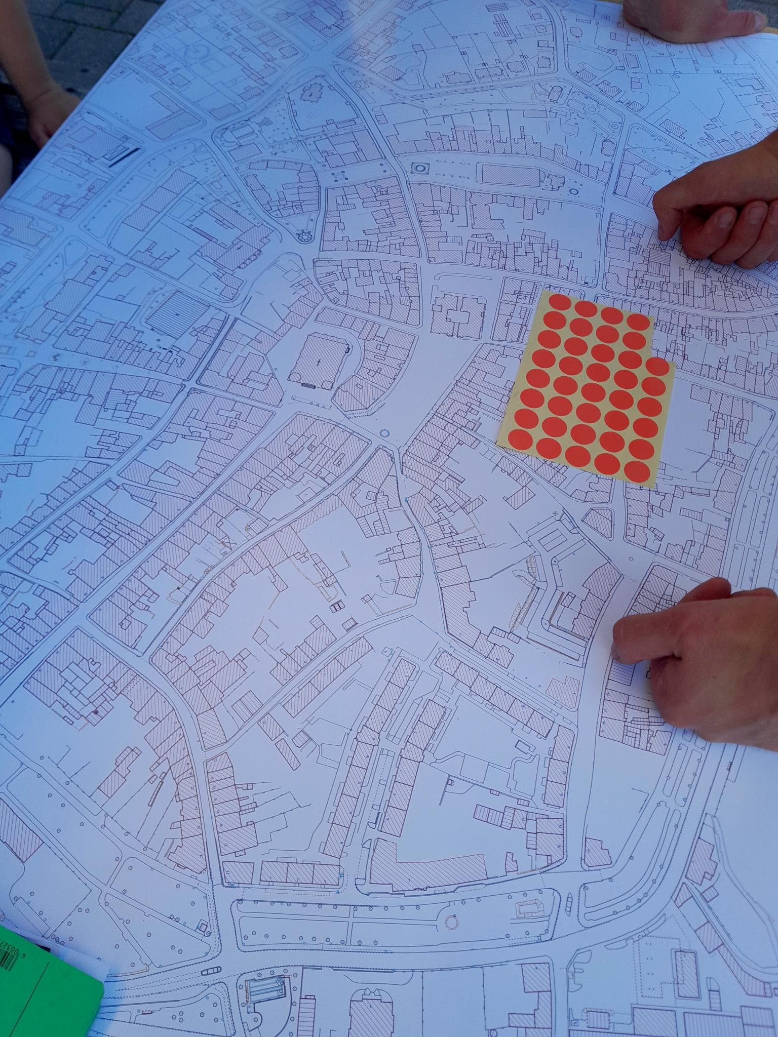 Foto eines technischen Stadtplans von Zittau auf einem Tisch. Mehrere Hände sind zu sehen. Auf dem Plan liegen rote Aufkleber bereit.