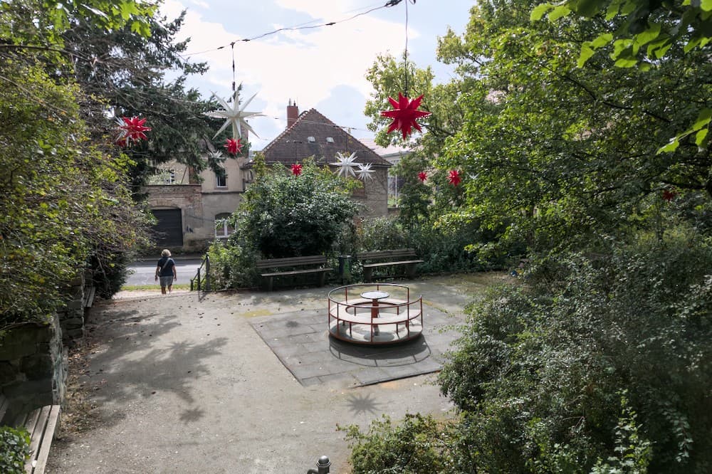 Rote und weiße Herrnhuter Sterne hängen über einem kleinen Platz, der von Pflanzen dicht umringt ist