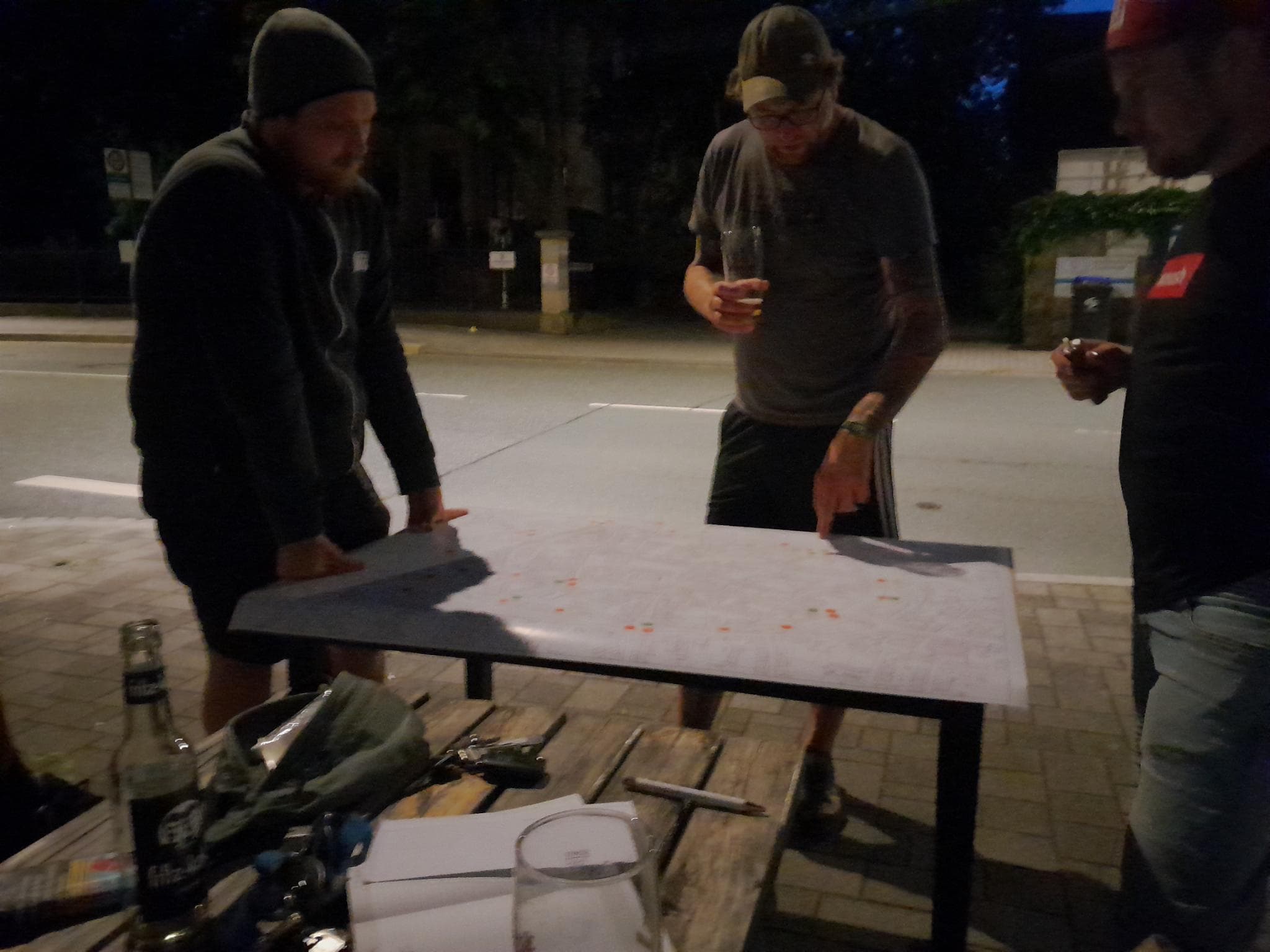 Foto eines Planungstreffens am Stadtring. Drei Personen stehen bei Dunkelheit und Licht einer Straßenlaterne um einen Tisch, auf dem ein großer Stadtplan mit roten Klebepunkten liegt