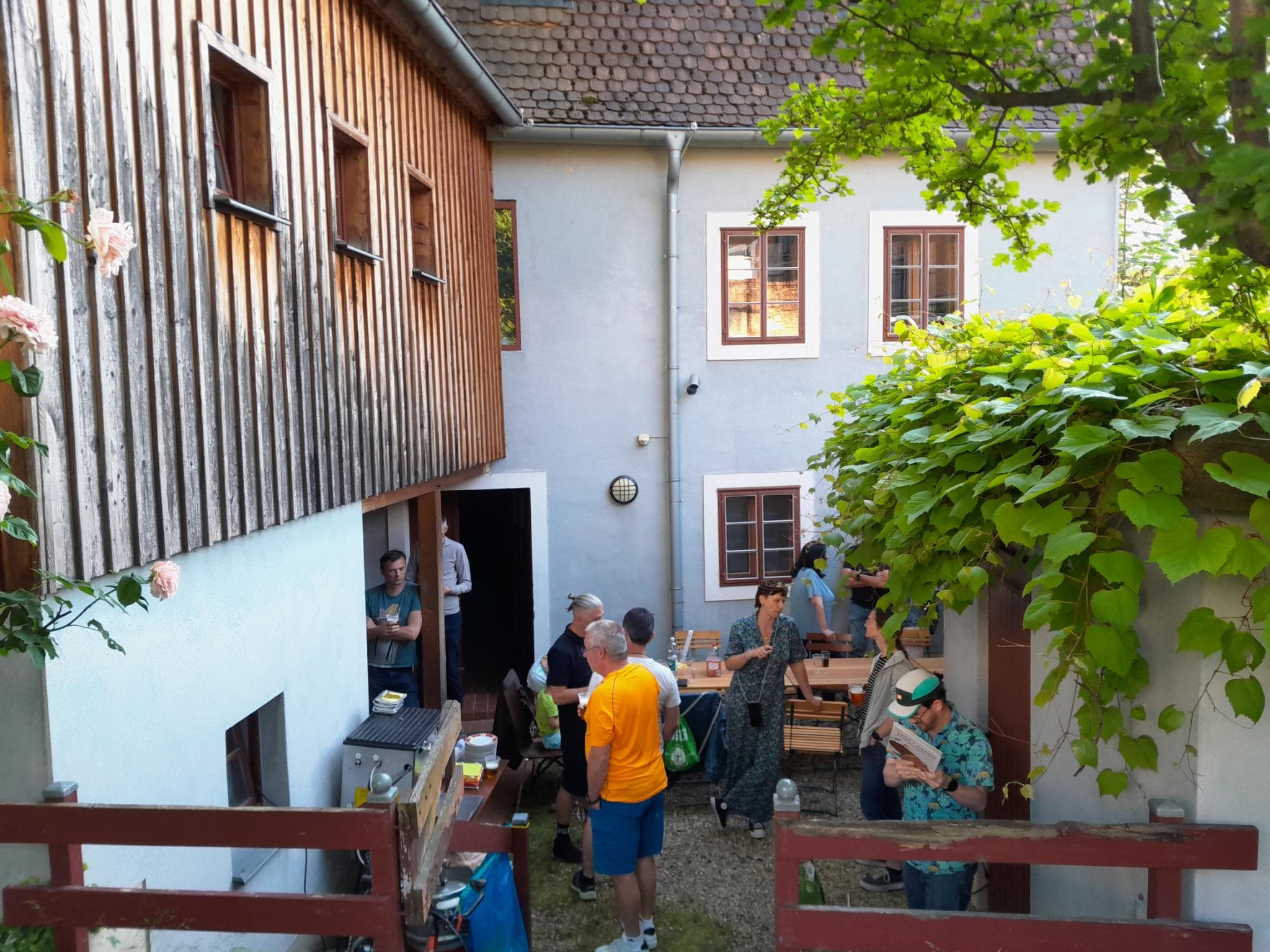 Foto einer Szene aus einem Garten hinter einem sanierten, mittelalterlichen Gebäude. Mehrere Personen stehen im Garten und sprechen oder bereiten eine Vereinssitzung vor.
